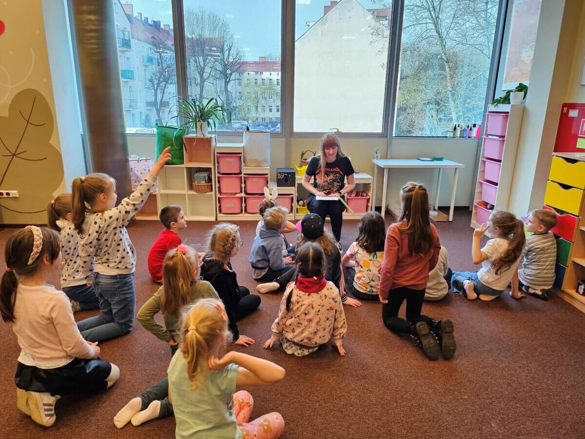 Dzieci w skupieniu słuchają książki czytanej przez Panią Bibliotekarkę.