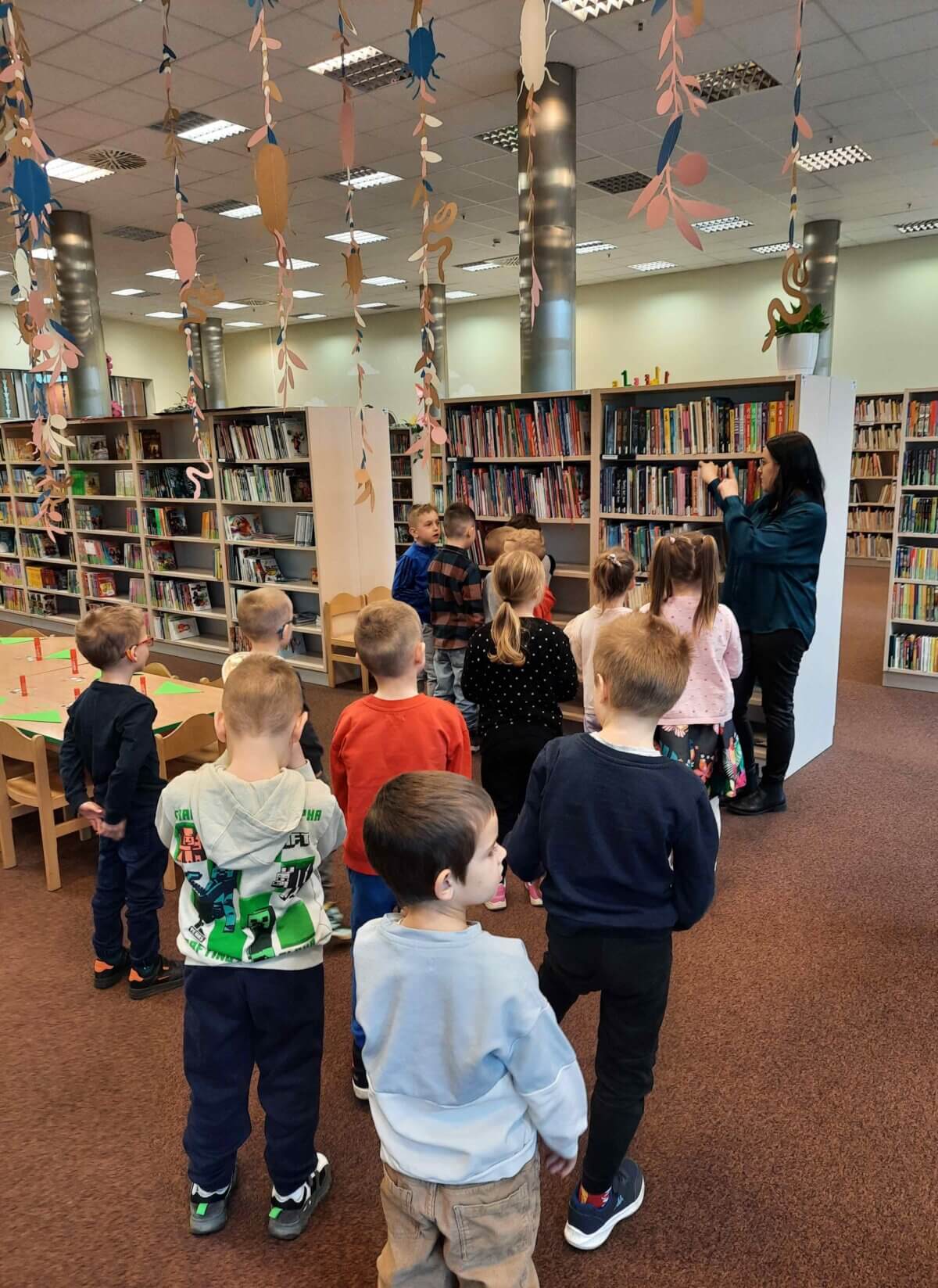 Pani Bibliotekarka oprowadza przedszkolaki po wypożyczalni dla dzieci.