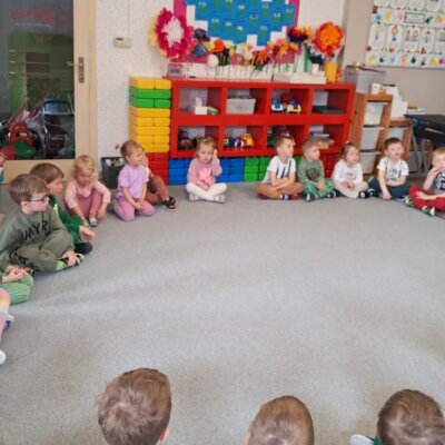 Dzieci siedzą w kole na dywanie, bibliotekarka pokazuje ilustracje. Kliknięcie powoduje powiększenie zdjęcia.
