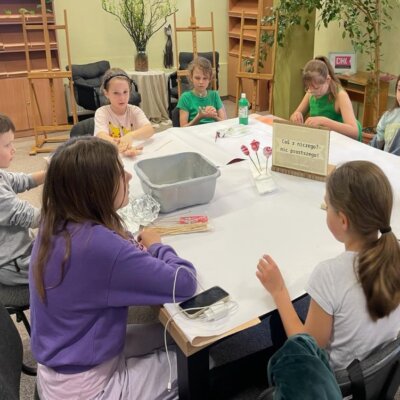 Dzieci siedzą przy stole. Ujęcie z innej strony. Kliknięcie powoduje powiększenie zdjęcia.