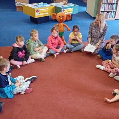 Dzieci siedzą w kółeczku na dywanie z bibliotekarką. Kliknięcie powoduje powiększenie zdjęcia.